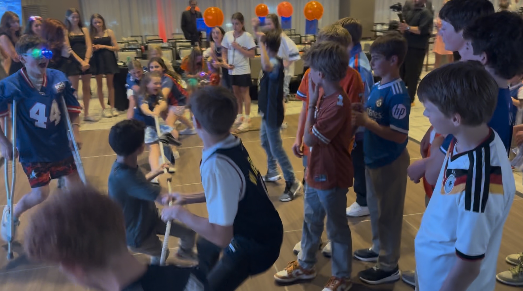 Hank's Basketball Themed Bar Mitzvah Group of kids playing tug-of-war at a party with colorful lights and balloons in the background.