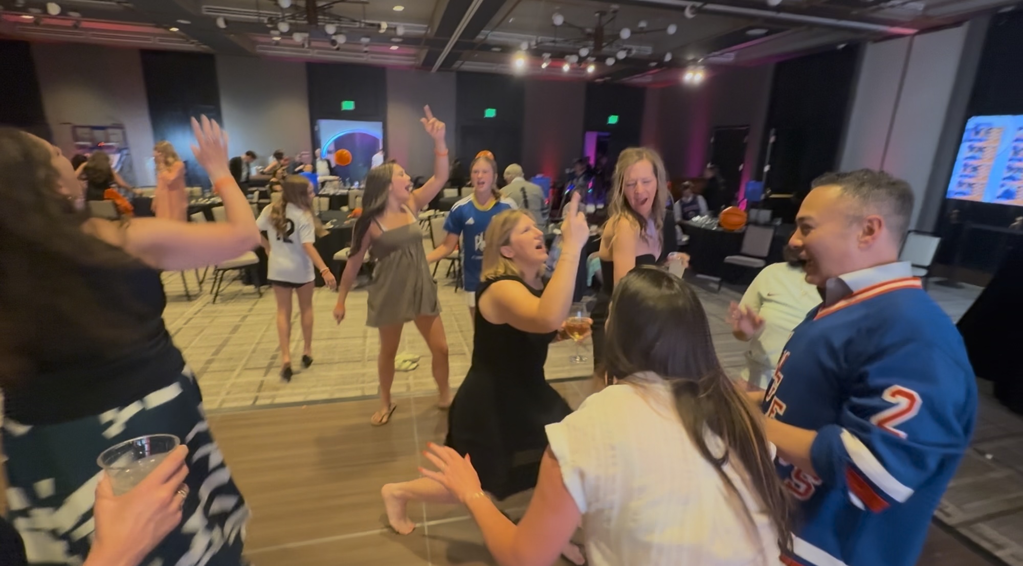 Screenshot Group of people dancing and celebrating at a party inside a banquet hall.