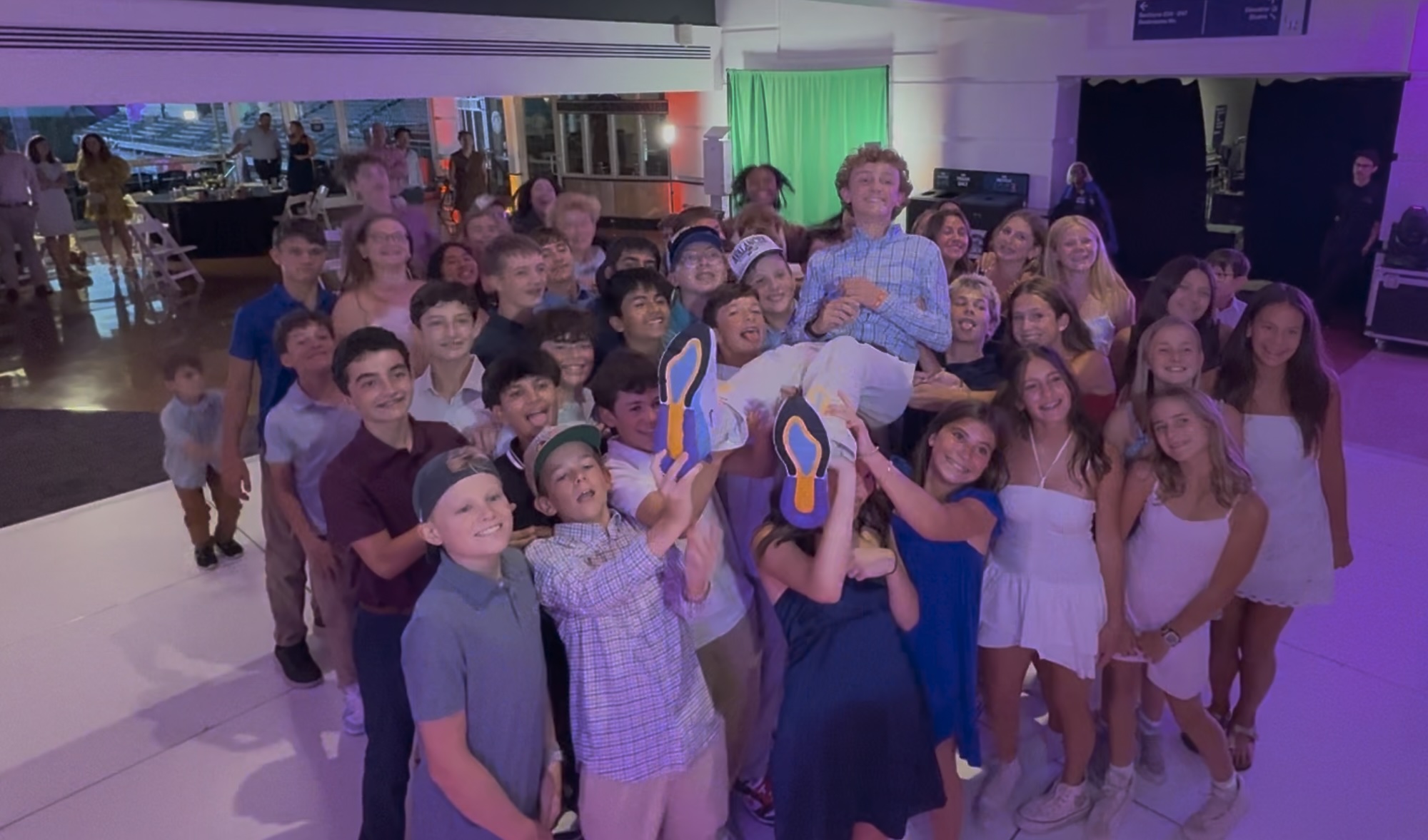 Group of young people celebrating at an indoor event, with one person being lifted in the air.